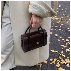 Close-up of wine red glossy leather square bag with gold COIN logo in autumn setting