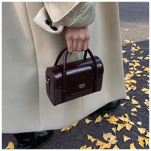 Detail of a dark brown glossy square handbag with gold COIN RDH logo in a street setting