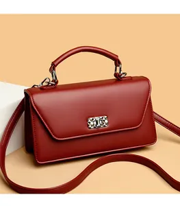 Detail view of burgundy leather square bag with silver clasp and top handle on a beige stand