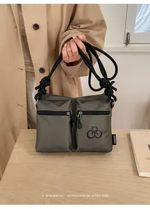 Detail of grey-green nylon crossbody bag featuring double front zip pockets and rope strap