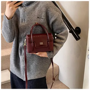 Detail of burgundy patent leather mini square bag with gold hardware and logo print
