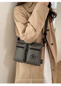 Olive nylon crossbody bag with dual zipper pockets shown on a beige trench coat