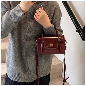 Close-up of wine red glossy leather crossbody bag with golden hardware and brand detail