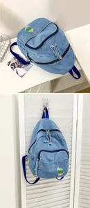 Détail du mini sac à dos en jean bleu avec broderie arc-en-ciel et fermetures à pompons