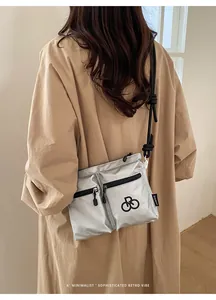 Close-up of metallic silver nylon crossbody bag with black rope strap on trench coat