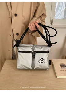 Close-up of silver nylon crossbody bag with dual front zippers and rope shoulder strap