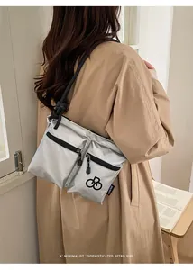 Rear view of silver nylon crossbody bag with black rope straps on beige trench coat