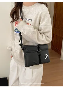 Detail of a black nylon crossbody tote bag showing dual zipper pockets and logo