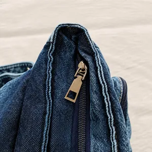 Detalle de cremallera de bronce y costura doble en mochila de mezclilla azul lavado