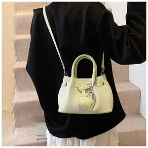Close-up of light green woven handbag with heart pendant and adjustable shoulder strap
