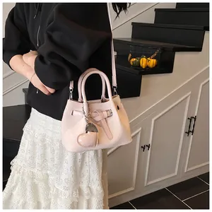 Detail of light pink woven bucket bag with heart pendant worn by a model in a modern room
