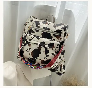 Detail of cow print PU leather backpack featuring golden zippers and striped woven strap