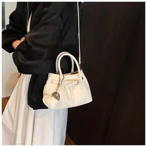 Detail of cream woven tote bag featuring adjustable leather straps and heart charm