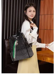 Détail d'un grand sac à dos noir brillant avec clous, poche latérale et pendentif ours