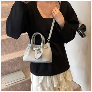 Detailed view of grey woven crossbody bag with heart charm shown on a model