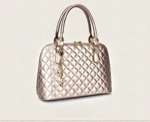 Detail view of champagne gold quilted shell bag with dual handles and metal butterfly charm