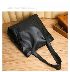 Flat lay of a black patchwork PU leather tote bag with geometric stitching on wood floor