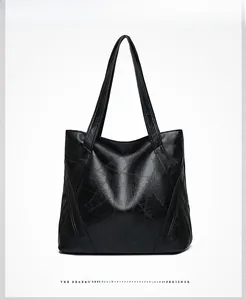 Detail view of the black tote bag showing glossy synthetic leather and geometric stitching