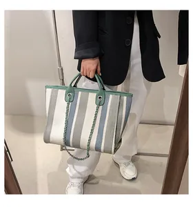 Detail of a large striped canvas bucket bag with green leather strap and chain