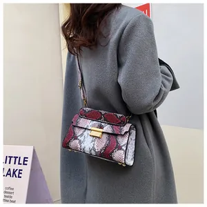Detail of red and grey snakeskin print crossbody bag with gold buckle on grey coat