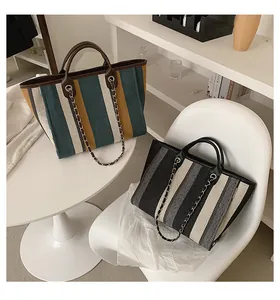 Detail of high-capacity striped canvas tote bags with leather trim and chain decoration