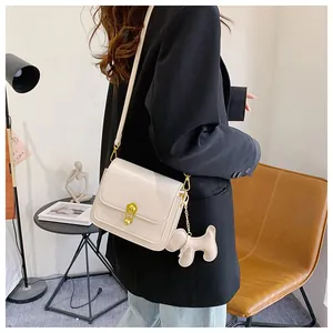 Close-up of minimalist cream square bag with gold clip lock and cute dog charm detail