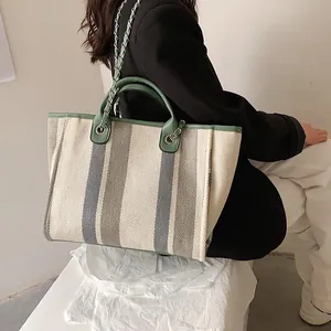 Chic striped tote bag with sage green trim and metal chain strap shown on model