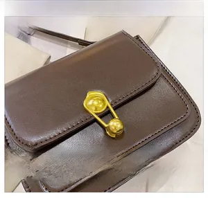 Close-up of a brown leather shoulder bag featuring a unique gold safety pin metal buckle