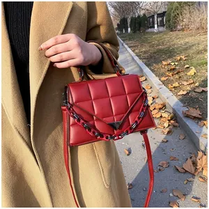 Fashionable dark red quilted handbag with metal triangle buckle worn with a camel coat