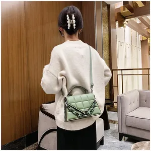 Detail of light green quilted handbag with black chain strap on a female model
