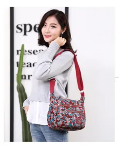 Detail of adjustable red strap and multi-zipper pockets on camouflage nylon crossbody bag