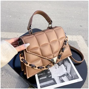 Detail of tan quilted handbag with chunky chain decor and triangular metal buckle