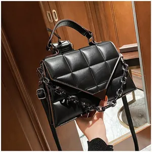 Detail of black quilted crossbody bag with metal chain and triangular flap cover