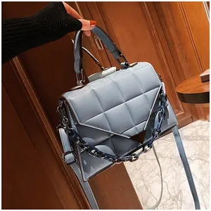 Detail of light blue quilted handbag featuring V-shape metal clasp and acrylic chain