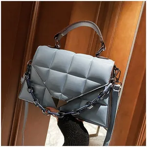 Close-up of light blue quilted leather bag with triangular buckle and resin chain detail
