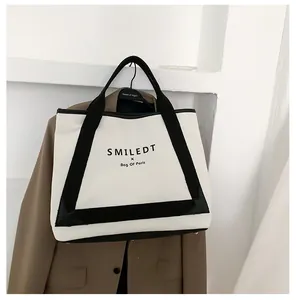 Vue détaillée du sac cabas en toile avec anses noires suspendu à une veste marron