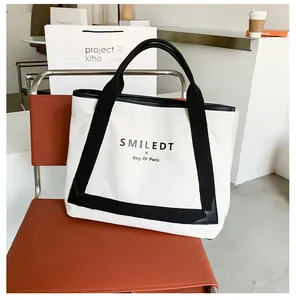 Détail d'un sac cabas en toile montrant les sangles logotées et la base renforcée sur une chaise