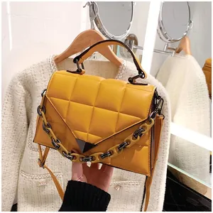 Detail of yellow quilted square bag with triangular metal lock and chain strap