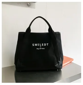 Détail du sac cabas en toile noire montrant le logo et le renfort d'angle en cuir