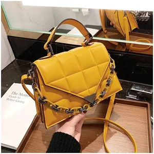 Detail view of yellow quilted handbag with V-shaped metal buckle and decorative chain