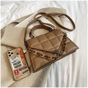 Detailed view of caramel brown quilted handbag with resin chain on beige coat