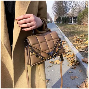 Detail of quilted crossbody bag with stylish chain strap and metallic triangle clasp