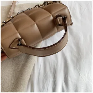Close-up of quilted brown leather handbag featuring fine stitching and metal chain detail