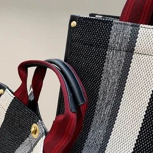 Detail of red and black striped webbing handle on a tweed patterned tote bag