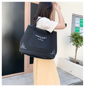 Détail du sac cabas en toile noire montrant le tissu épais et le socle en cuir robuste