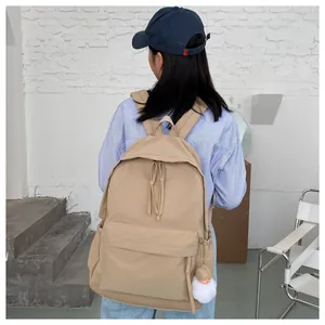 Detail of khaki campus backpack with zipper pulls and white plush ball charm