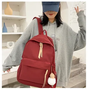 Detail of dark red canvas backpack with cream ribbon zippers and white plush pendant