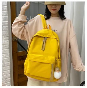Detail view of bright yellow canvas backpack with front pocket and decorative girl pendant