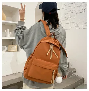 Detailed back view of a caramel student backpack with a soft white plush ball charm