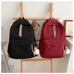 Detail of minimalist canvas backpacks in black and burgundy with plush pendant and long tassels